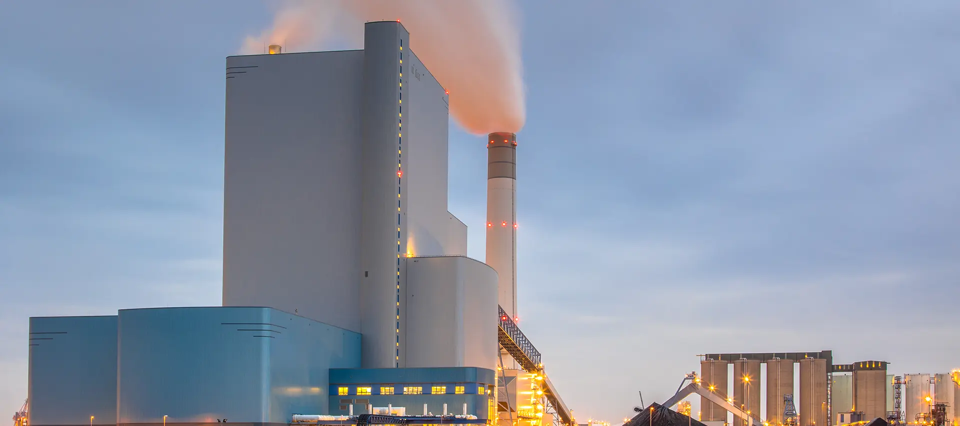 Una central eléctrica con una gran chimenea y una torre de refrigeración al fondo.
